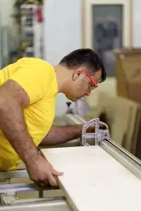 carpenter-cutting-piece-wood-furniture-his-woodwork-workshop-using-circular-saw-wearing-safety-goggles